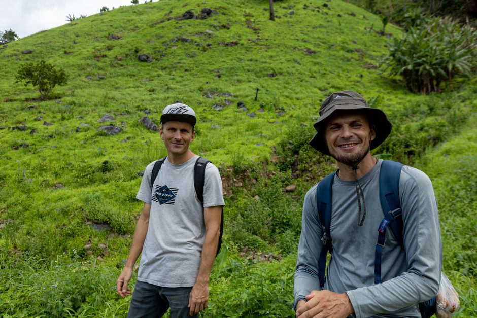Two men enjoying a hike in a rural green hillside, capturing the essence of outdoor adventure.