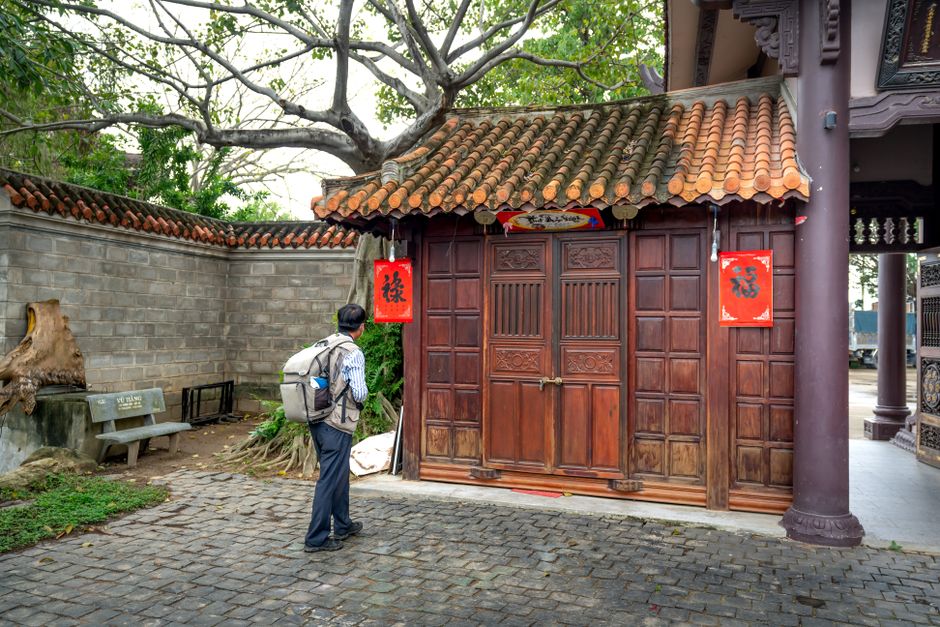 An adult man with a backpack observes a traditional Chinese building with ornate wooden doors.