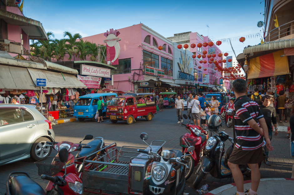 Lively street scene with bustling market, vehicles, and lanterns in an Asian city.