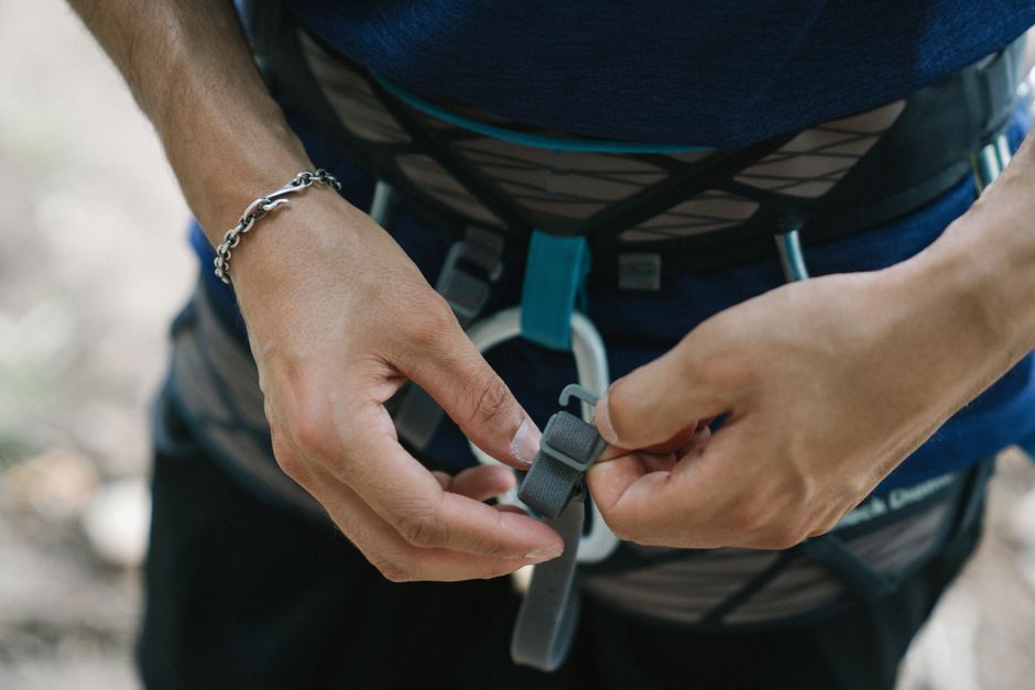 Detail of a person securing a climbing harness, focusing on safety gear and technique.