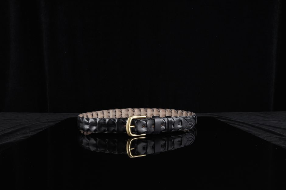 Stylish black leather belt with a gold buckle elegantly displayed on a reflective black surface.