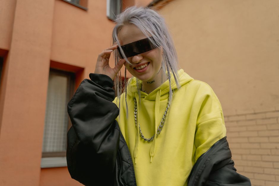 Woman with sunglasses in a yellow hoodie smiling outdoors, embodying urban street style.
