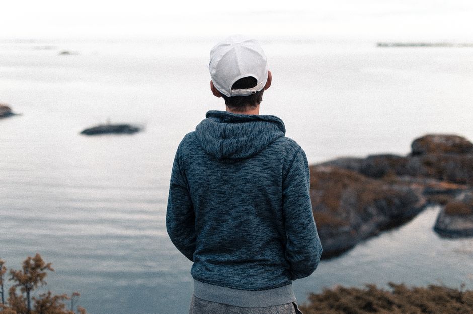 A young person stands alone overlooking a calm sea with rocky islands on a tranquil day.