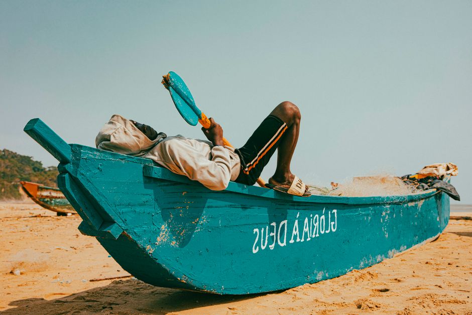 A person relaxing on a colorful blue boat on a sunny beach, exuding a sense of calm.