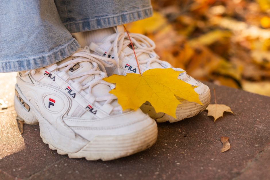 Close-up of white sneakers with a yellow maple leaf on them, symbolizing fall.