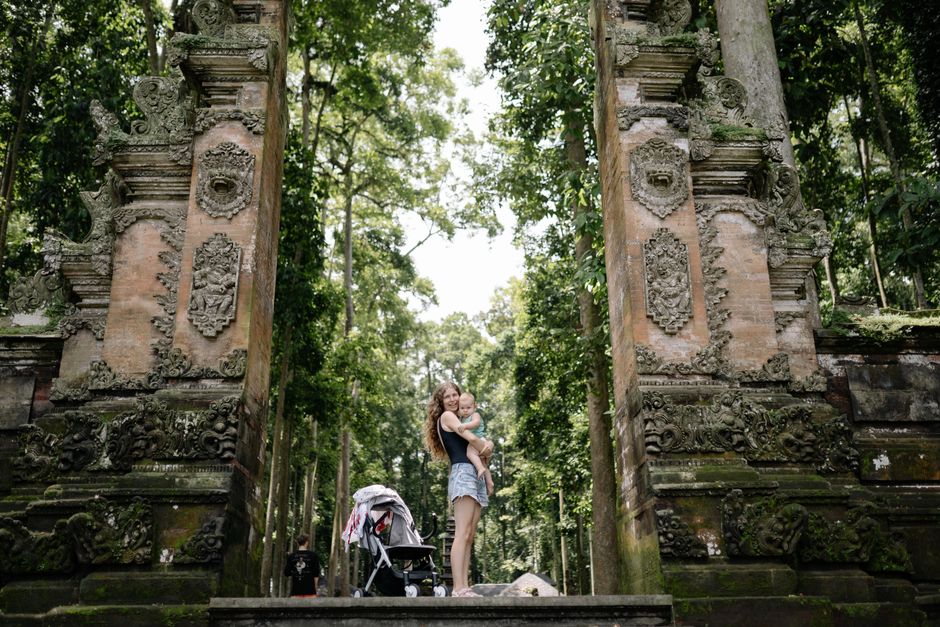 A mother and child stand by an ancient temple gate surrounded by lush greenery.