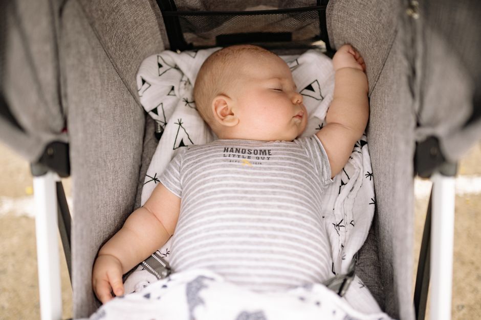 Adorable baby peacefully sleeping in a stroller, wearing a striped onesie.