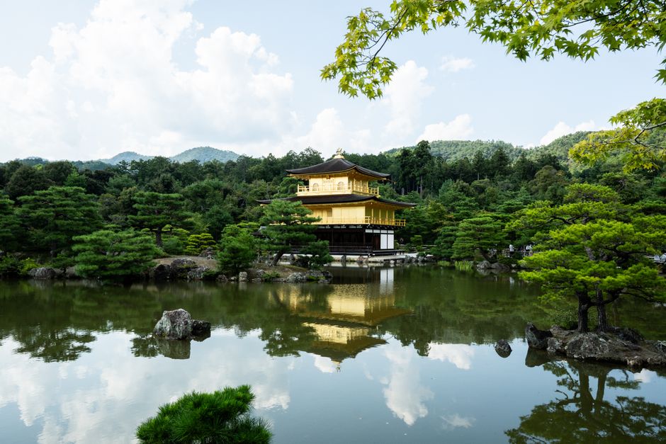 The picturesque Kinkaku-ji Temple in Kyoto reflected in a tranquil pond surrounded by lush greenery.