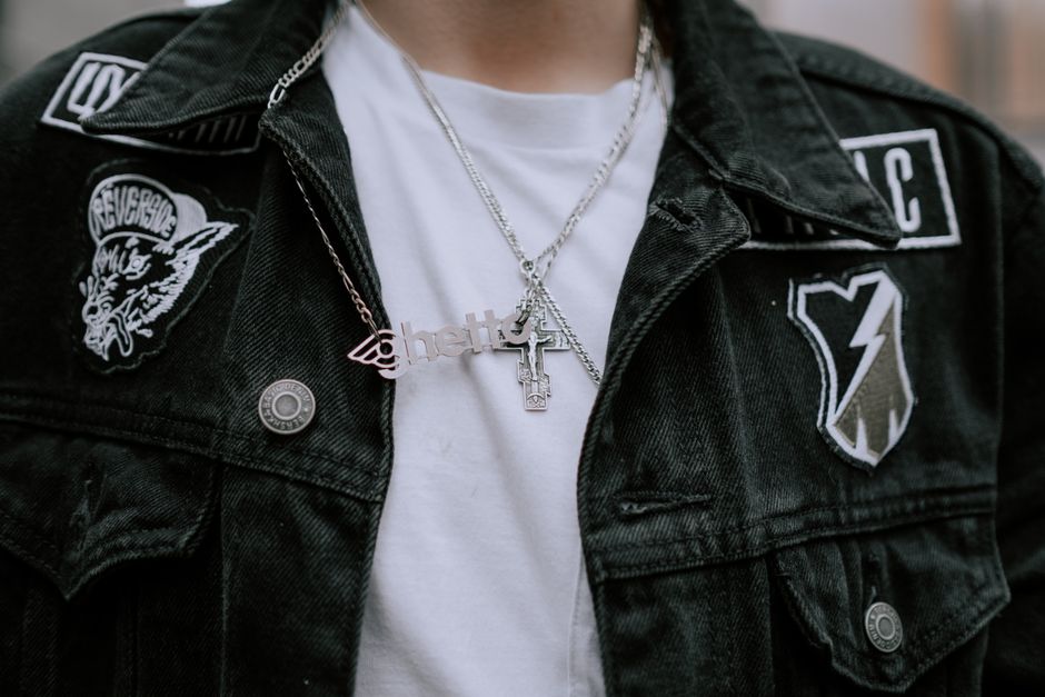 Close-up of black denim jacket with stylish patches and cross pendant necklaces, showcasing urban fashion.