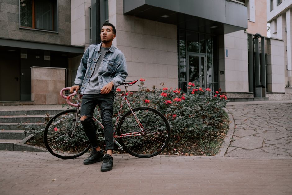 Stylish man leaning on his road bike next to vibrant roses outside modern buildings.