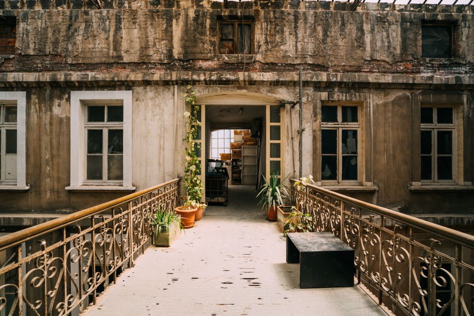 An abandoned building exterior with plants and vintage railings in an urban setting.