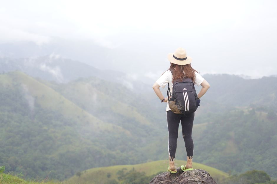 A woman stands on a rock, overlooking a misty mountain landscape, embodying adventure.