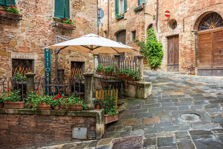 Charming view of a medieval alleyway in Montepulciano, Italy, featuring rustic buildings and a café.