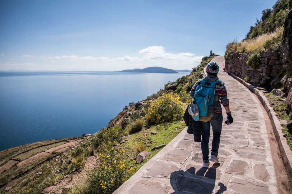 A woman hikes along a path by Lake Titicaca in Bolivia, enjoying a sunny day.