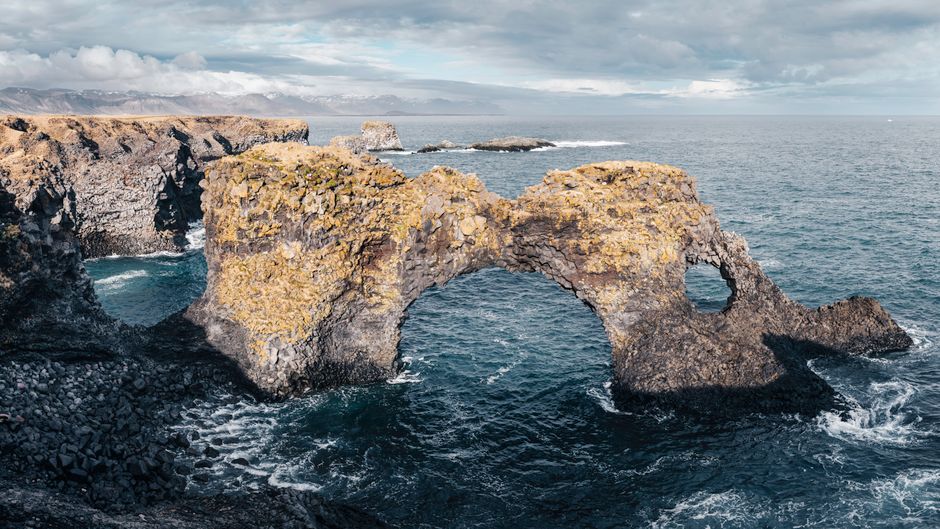 Stunning view of a natural rock arch along the Icelandic shoreline against a vast ocean backdrop.