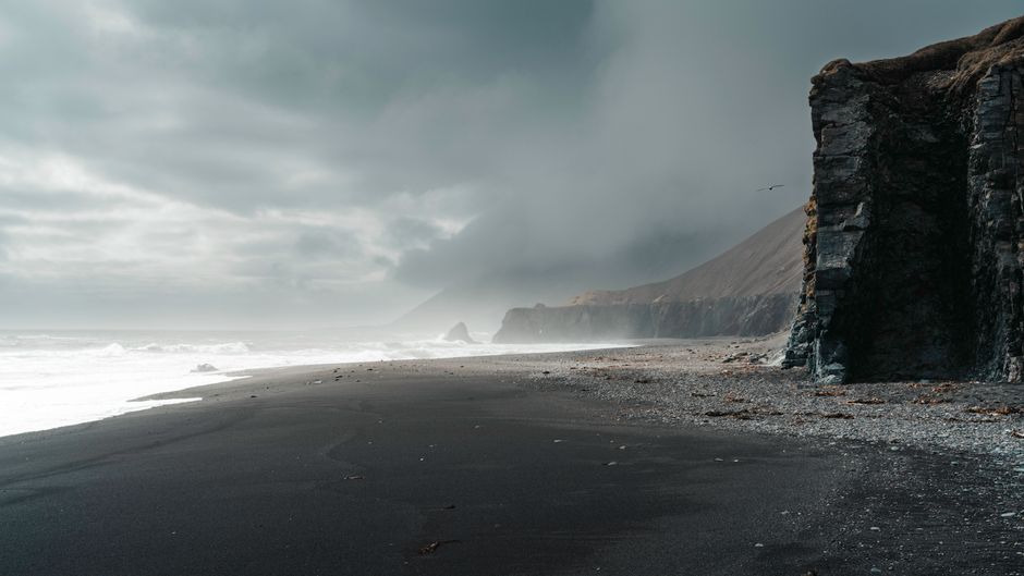 Moody seascape with black sand beach, cliffs, and dark clouds in Iceland.