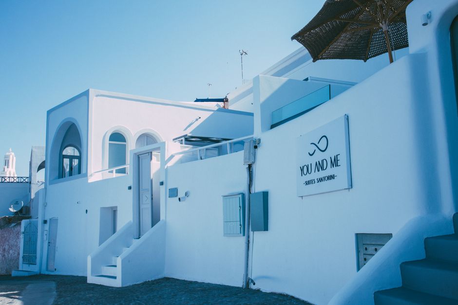 Charming exterior view of a Santorini hotel with iconic white architecture and arched windows under a clear blue sky.