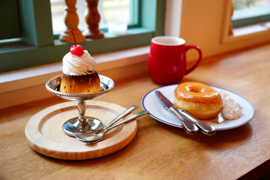 Delicious pudding and glazed doughnut on a wooden table with coffee in a cozy café setting.