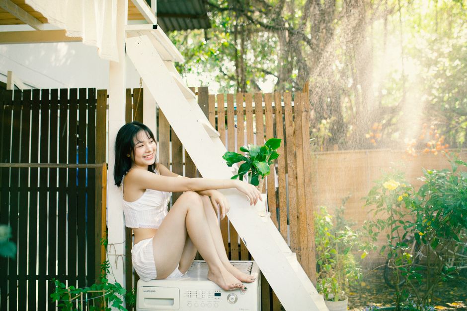 A young woman smiles sitting outdoors in summer next to laundry drying.