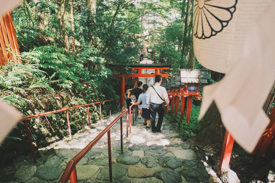 Visitors descend the stone steps of Kifune Shrine in Kyoto, surrounded by lush greenery and traditional architecture.