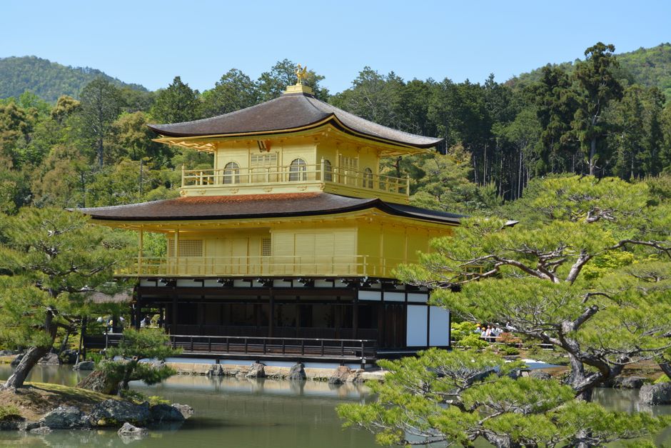 The iconic Kinkaku-ji Temple in Kyoto, Japan, reflected in a tranquil pond surrounded by lush forest.