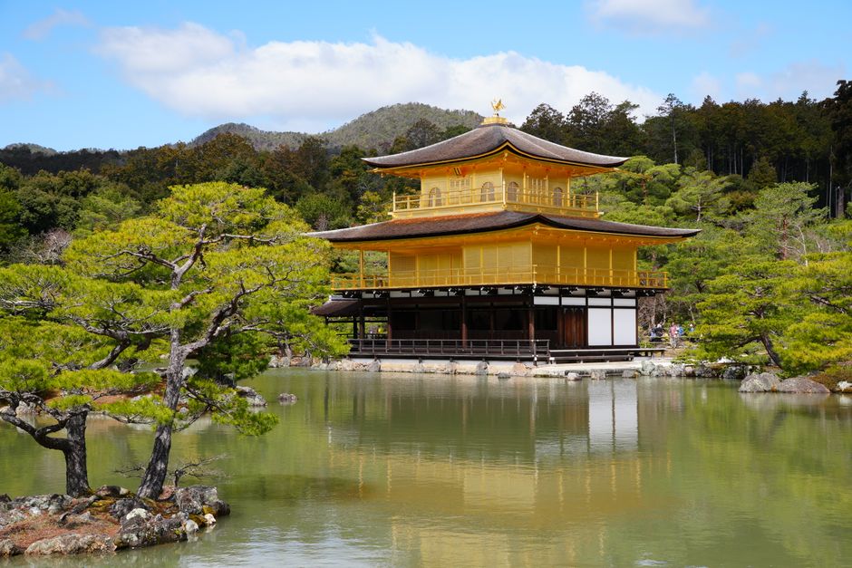Kinkaku-ji Temple in Kyoto, Japan, reflected in a serene lake amidst lush greenery.