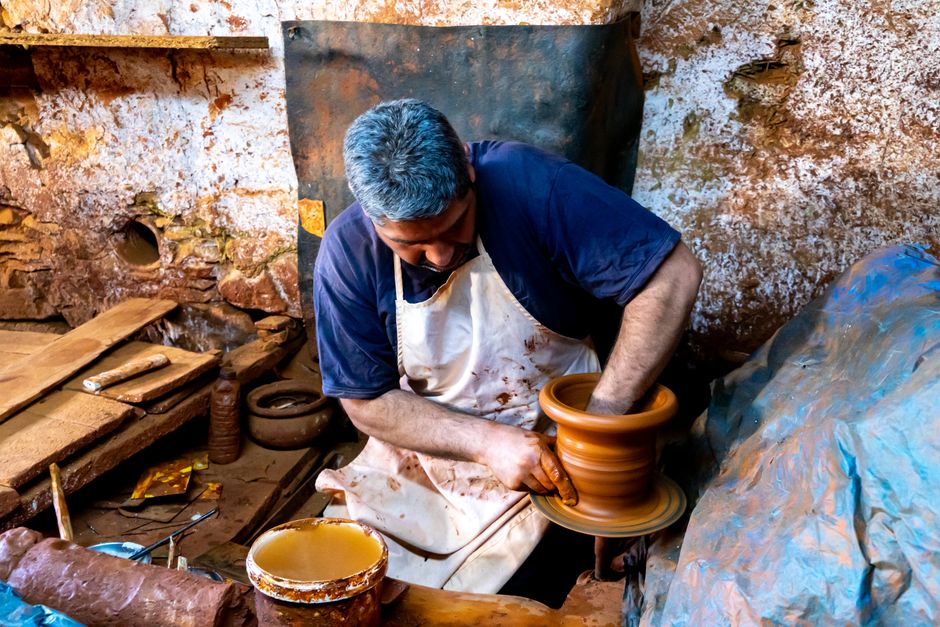 A potter skillfully shapes a clay pot on a wheel in a rustic workshop, showcasing craftsmanship.