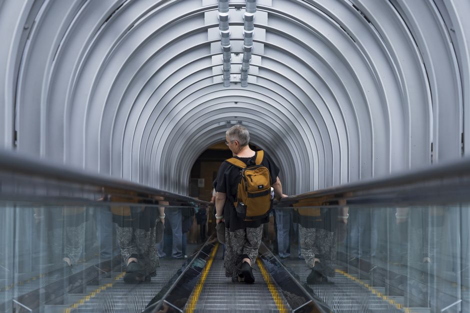 Traveler with a backpack descends an escalator inside a futuristic tunnel.