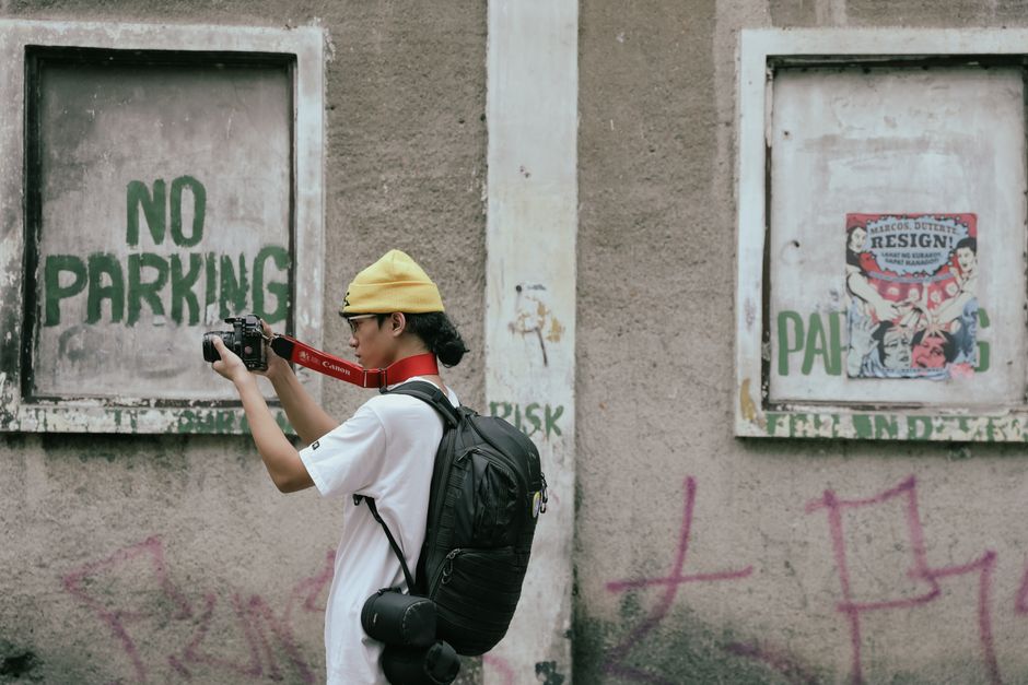 A photographer takes a picture of street art against a worn urban wall.