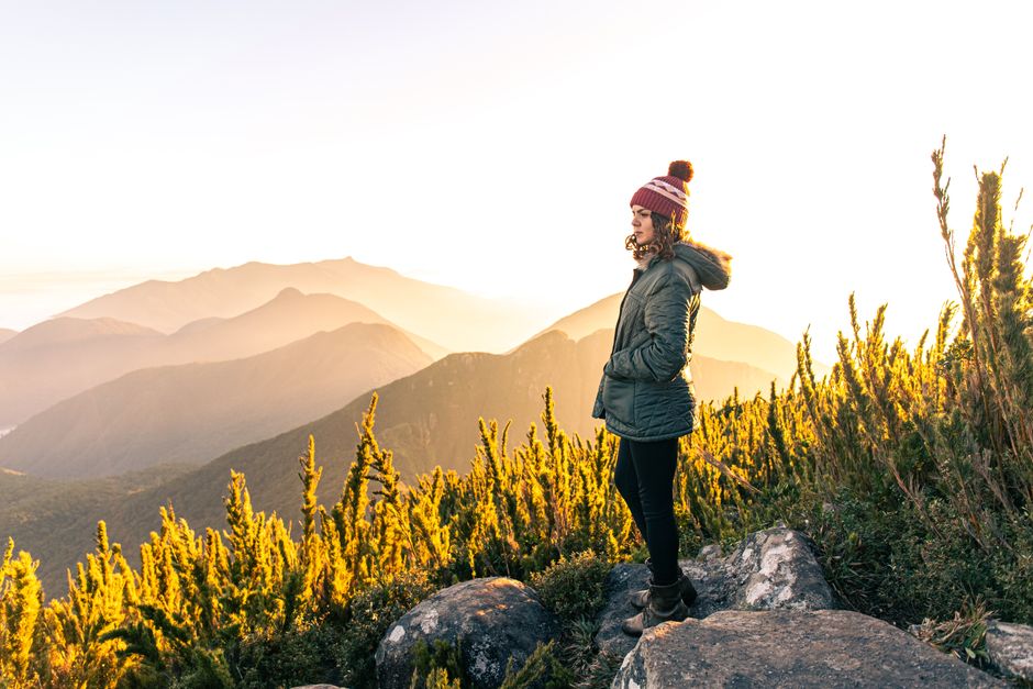 A woman enjoys a sunrise hike on a Brazilian mountain, surrounded by lush greenery.