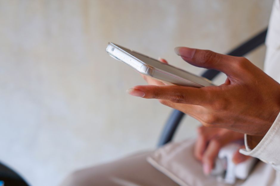 A close-up image of a person holding a smartphone while indoors, focusing on hand details.