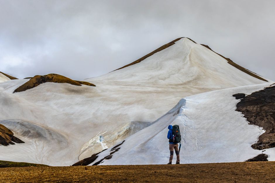 Hiker with backpack navigates snowy slopes of rugged mountain under overcast sky. Adventure in Iceland.