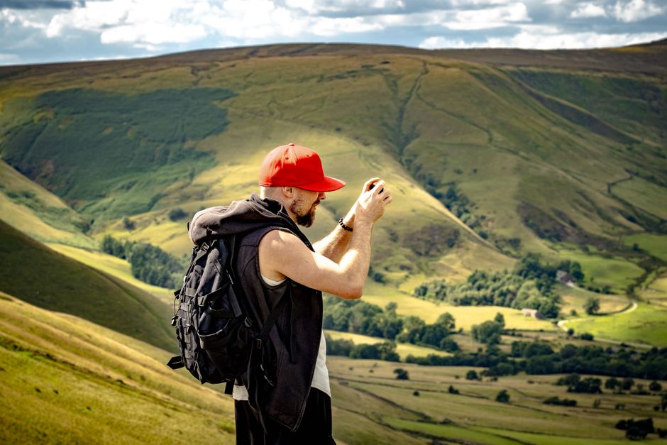 Man takes photos in a picturesque hilly countryside setting, ideal for travel and nature themes.