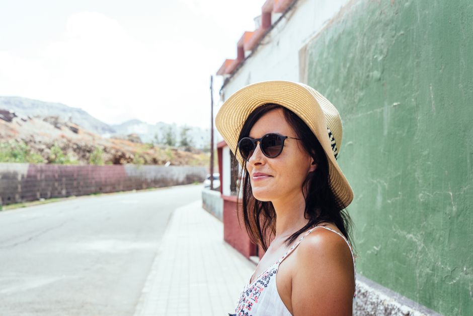 A woman in a sun hat and sunglasses smiles on a summer day in Spain.