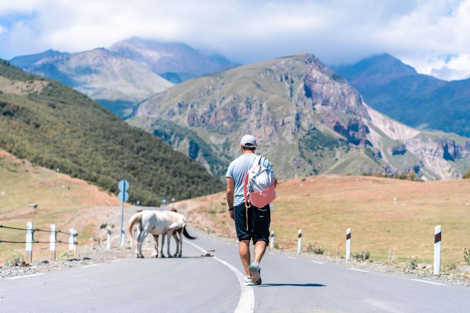 Traveler walking on scenic mountain road in Stepantsminda, Georgia.