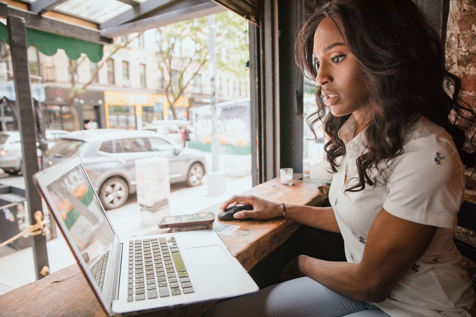 Businesswoman using laptop at window-side table in urban cafe.