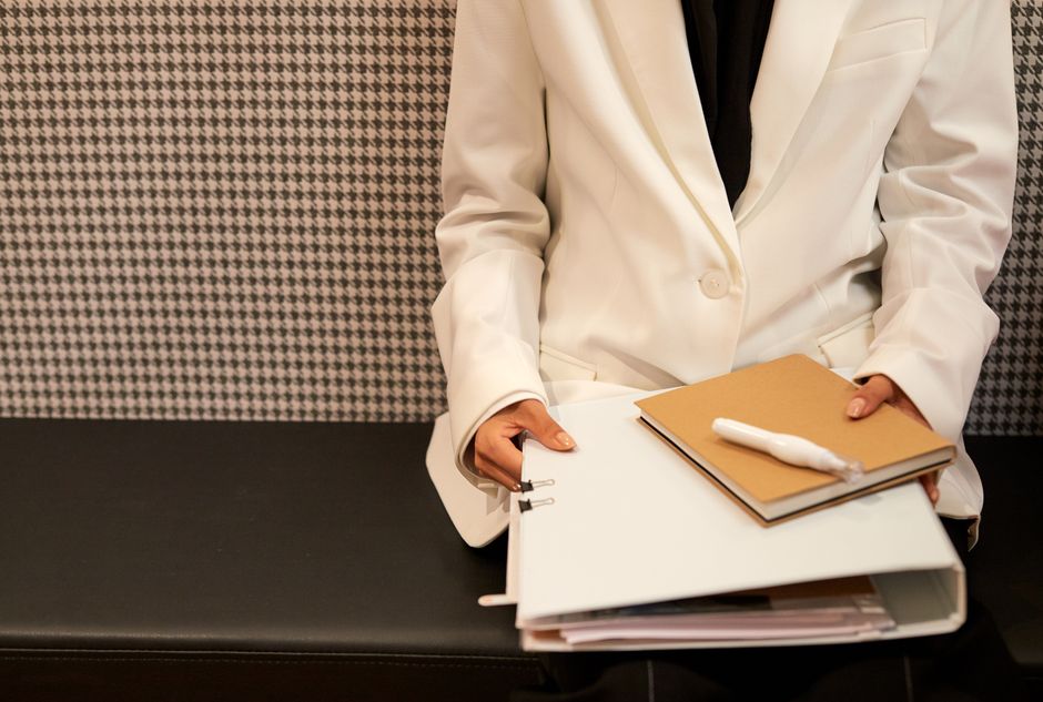 Close-up of a business professional in a white suit holding documents in a modern office setting.