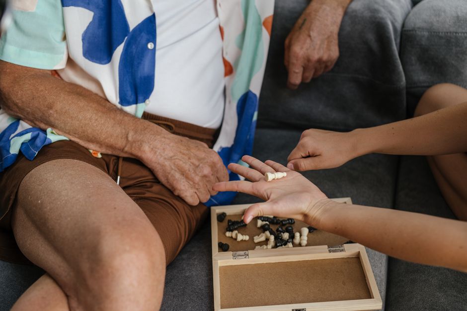 An elderly man and young adult sharing a bonding moment over a game of chess indoors.