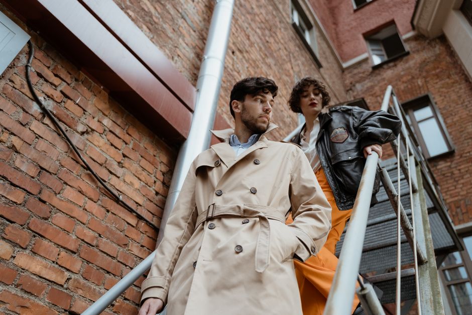 Stylish man and woman descending outdoor metal stairs against a brick wall.