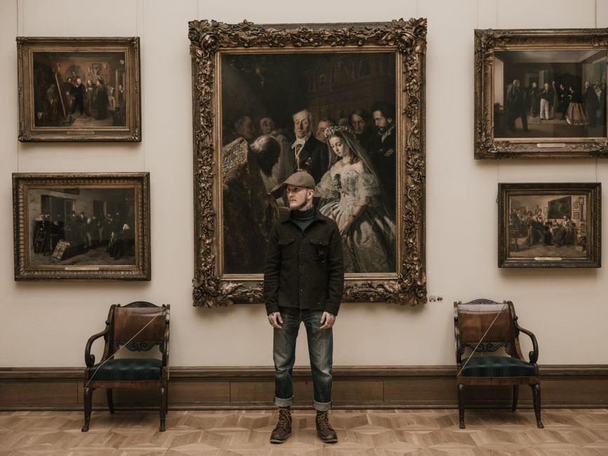 A man stands in a museum gallery surrounded by vintage paintings.