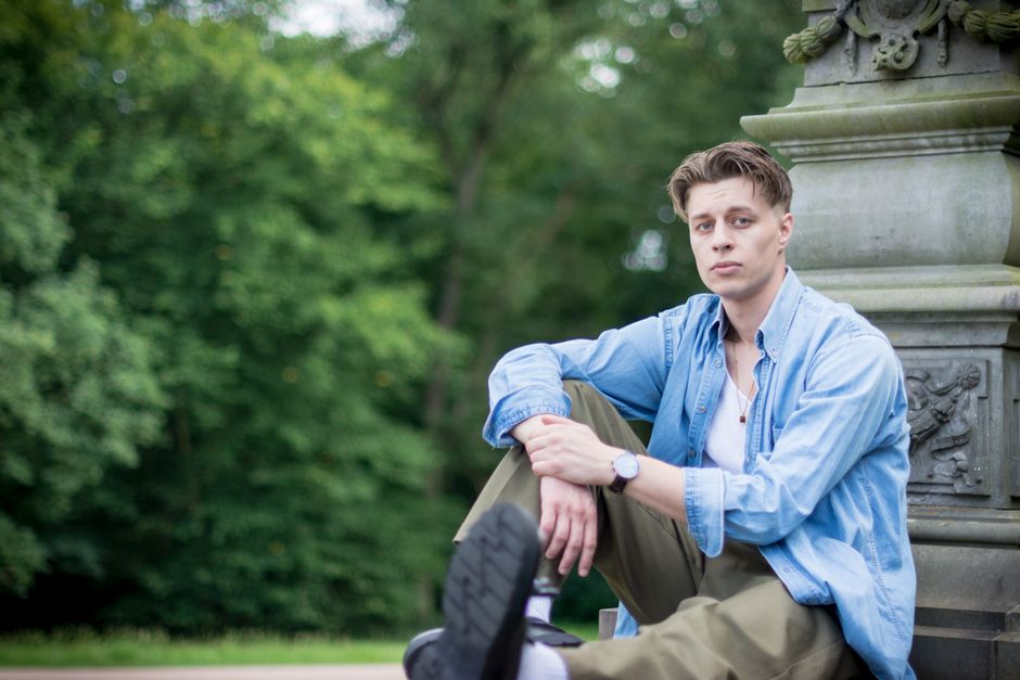Young man in casual attire posing thoughtfully outdoors by a monument in a park.