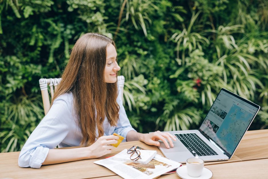 Young woman sitting at a table with a laptop and coffee, enjoying outdoor workspace.